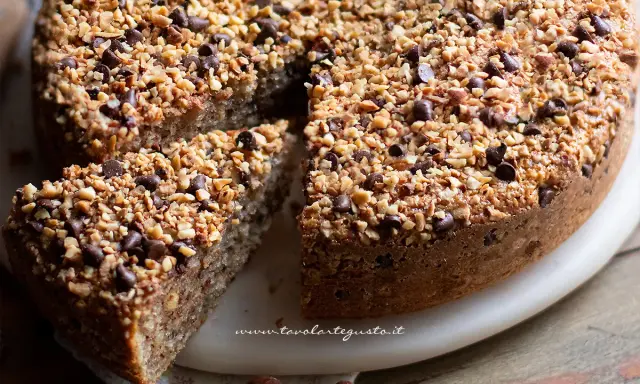 Una deliziosa torta di nocciole, ricoperta di granella di nocciole e gocce di cioccolato, con una fetta tagliata.