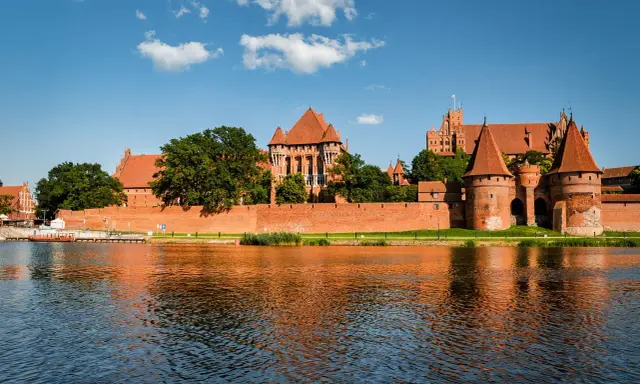 Potężny zamek w Malborku odbija się w wodzie. Zastanawiasz się, ile trwa zwiedzanie zamku w Malborku?