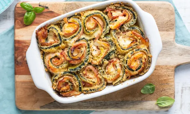 Involtini di zucchine al forno, ripieni di prosciutto e formaggio, dorati e croccanti, guarniti con basilico fresco.