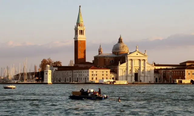 Le campanile et l'église de San Giorgio Maggiore à Venise se reflètent sur l'eau. Un bateau transporte des passagers.