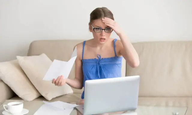 Zmartwiona kobieta z okularami sprawdza dokumenty na laptopie, martwiąc się o przedawnienie długu za czynsz mieszkaniowy.