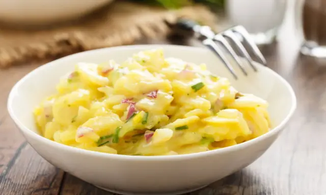 Schüssel mit cremigem Kartoffelsalat, garniert mit roten Zwiebeln und Schnittlauch. Ein köstliches Rezept für Kartoffelsalat!