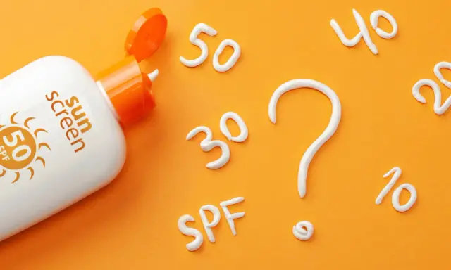 Flacon de crème solaire SPF 50 ouvert, avec des chiffres (30, 40, 20, 10) et un point d'interrogation formés en crème. Quel indice choisir ?