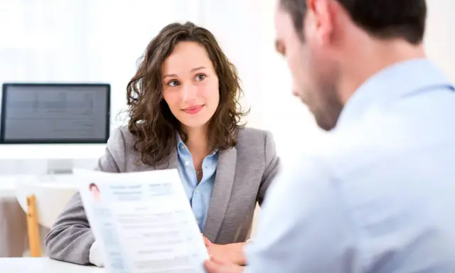 Kobieta z uśmiechem słucha podczas rozmowy kwalifikacyjnej po angielsku. Przed nią leży CV.
