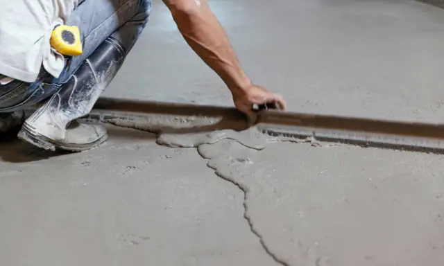 Obrero con botas y cinta métrica trabajando en como nivelar un suelo de cemento con una regla de albañil.