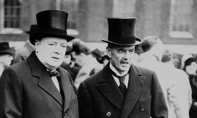 Winston Churchill und Neville Chamberlain, die die Appeasement-Politik kritisierten, tragen Zylinder.