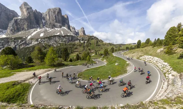 Ciclisti affrontano tornanti in una spettacolare salita alpe d'Huez, con maestose montagne sullo sfondo.