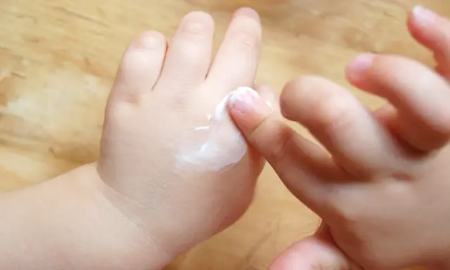 Mani di bambino applicano crema, un gesto che aiuta a contrastare la pelle atopica, alleviando secchezza e prurito.