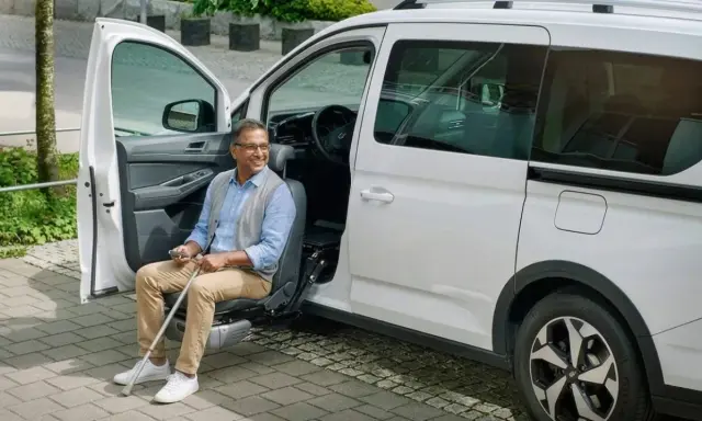 Hombre sonriente sentado en un asiento elevador de coche, listo para salir. Un ejemplo de soluciones de movilidad accesibles.