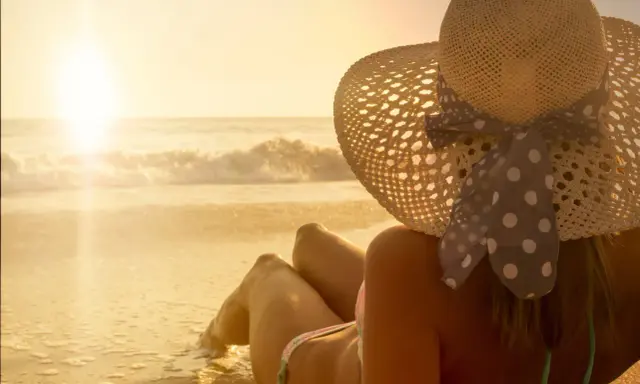 Donna con cappello di paglia sulla spiaggia, godendosi il sole per un'abbronzatura perfetta.