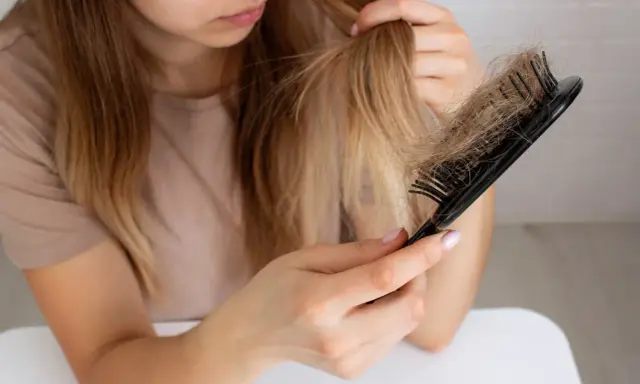 Donna preoccupata guarda i capelli persi sul pettine, chiedendosi perché perdo capelli.