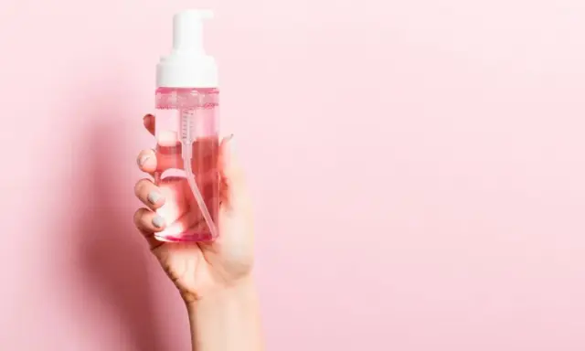 Mano sostiene botella de agua micelar con dispensador. ¡Perfecto para cuando el agua micelar se enjuaga!