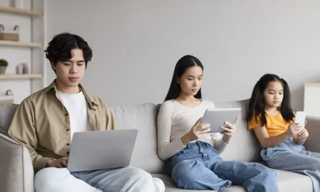 Trois personnes sur un canapé : un jeune homme sur un ordinateur portable, une femme sur une tablette, et une jeune fille sur un smartphone. Le temps d'écran recommandé pour 13 ans est dépassé pour certains.