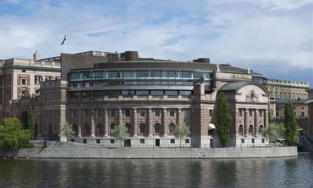 Riksdagshuset i Stockholm, en symbol för sveriges statsskick, med sin moderna glasdel och klassiska stenfasad vid vattnet.