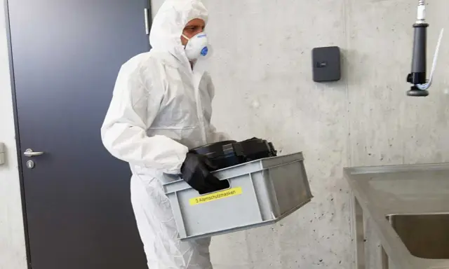 Hombre con traje blanco y mascarilla, lleva caja con equipo de protección obligatoria de vías respiratorias.
