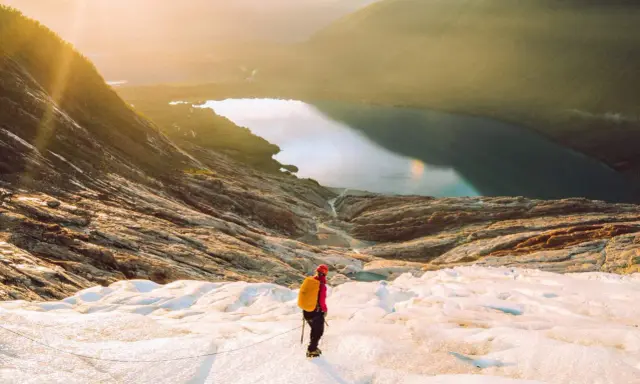 Vandrare på en glaciär i Norge med en sjö och berg i bakgrunden. En av många norge sevärdheter.