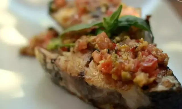 Deliciosa corvina a la plancha con un sofrito de tomate y hierbas frescas, servida en un plato blanco.