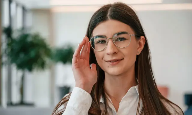 Uśmiechnięta kobieta w okularach do czytania i chodzenia poprawia oprawki.