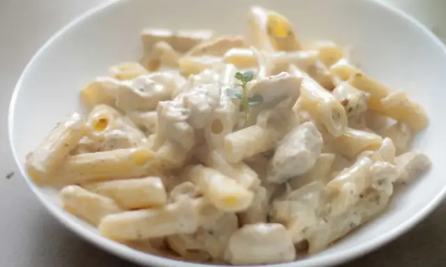 Penne z kremowym sosem i kawałkami kurczaka, udekorowane gałązką ziół. Pyszna potrawka z kurczaka w sam raz na obiad.