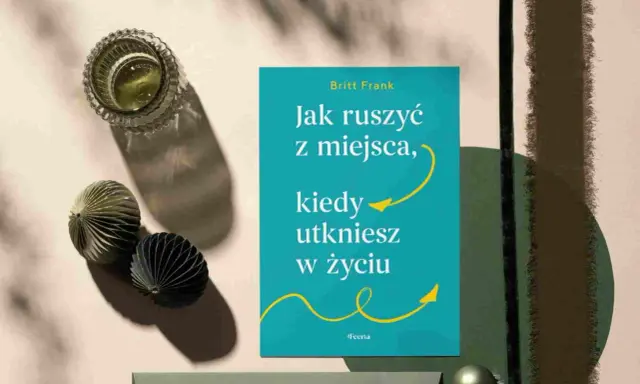 Książka "Jak ruszyć z miejsca, kiedy utkniesz w życiu" Britt Frank. Obok szklanka z napojem i ozdobne kule. Idealna lektura, gdy dopada lenistwo.