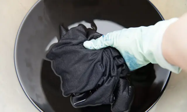 Mano con guante sumerge ropa blanca desteñida de negro en tinte oscuro.