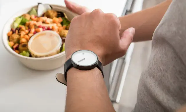 Mann schaut auf seine Uhr, neben einer Schüssel mit Salat. Die Frage: darf man fasten wenn man krank ist?
