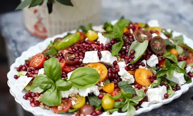 En färgglad sallad med granatäpple, tomater, fetaost och basilika, perfekt som sallad till grillat.