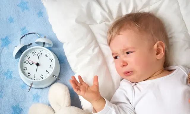Płacz 1,5 rocznego dziecka, które nie chce spać w dzień. Obok budzik i pluszaki.
