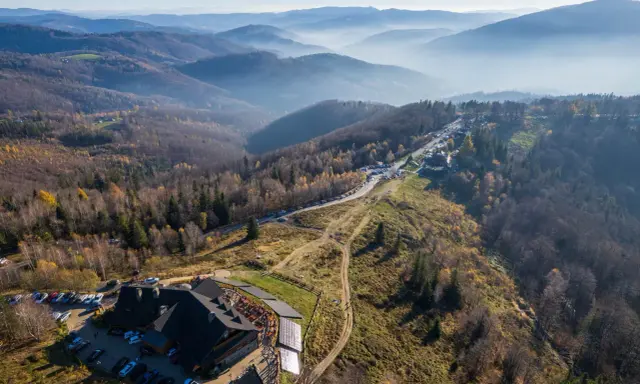 Widok na górskie krajobrazy i architekturę w Ustroniu. Widać parkingi, budynek z drewnianą architekturą i szlaki turystyczne.