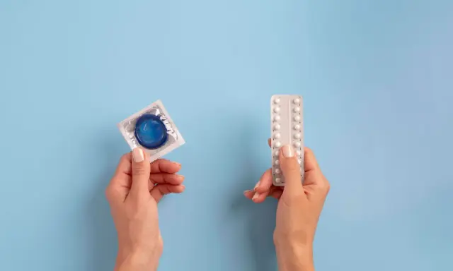 Manos sostienen un preservativo y pastillas anticonceptivas, mostrando opciones de planificación familiar.