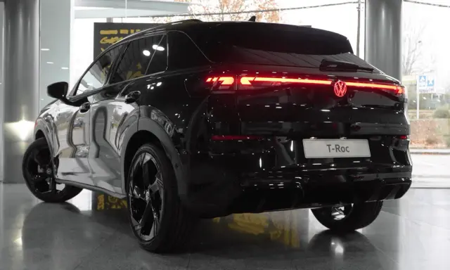 El Volkswagen T-Roc 2026 negro brillante, con sus luces traseras LED rojas encendidas, se exhibe en un concesionario.