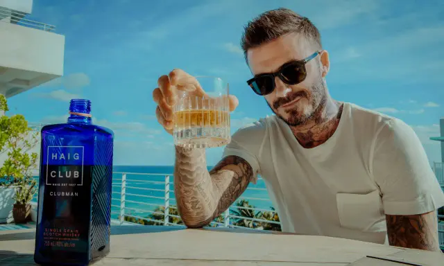 David Beckham z kieliszkiem Haig Club whisky, na tle błękitnego nieba i morza. Idealny moment na relaks.