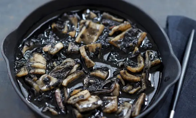 Calamares en su tinta, un plato oscuro y sabroso, servido en una sartén de hierro fundido.