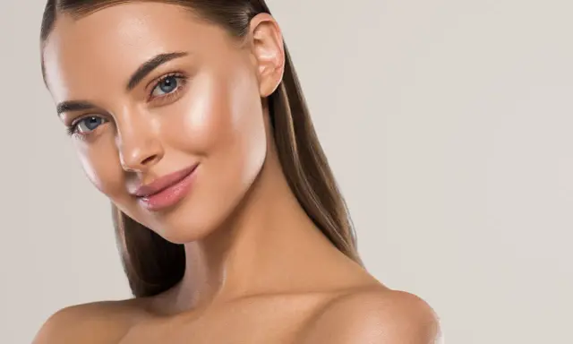 Visage d'une femme au teint hâlé, avec des yeux bleus et des lèvres roses. Elle sourit légèrement, suggérant une peau parfaite pour comment bronzer rapidement.