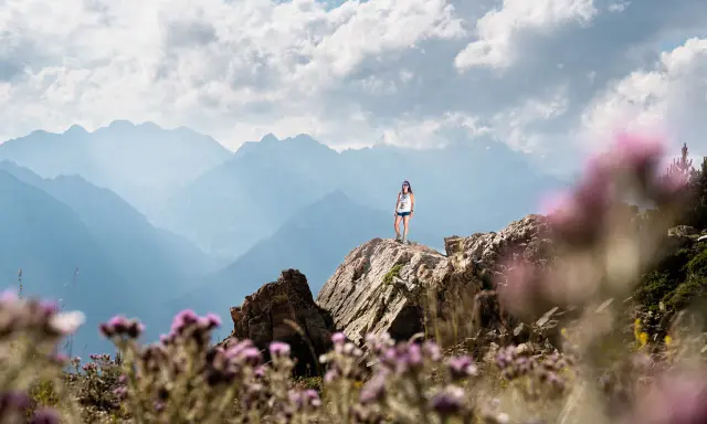 Una mujer en la cima de una montaña rocosa, disfrutando de las vistas. ¡Una gran idea de qué hacer en Cerler en verano!