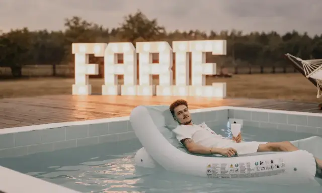 Relaks przy basenie z drinkiem, wielkie litery "FARTE" w tle. Idealny pomysł, jak zorganizować wieczór kawalerski.