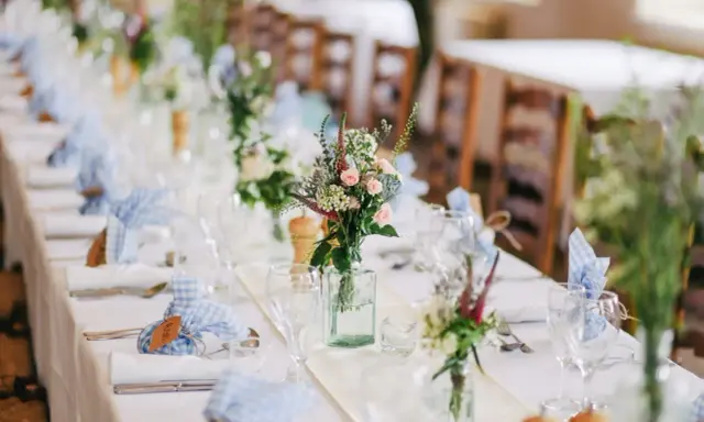 Disposition des couverts à la française sur une longue table dressée pour un événement, avec des fleurs sauvages et des serviettes à carreaux bleus.