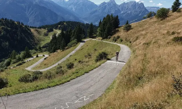 Radfahrer kämpft sich die Serpentinen des Monte Zoncolan hoch. Majestätische Berge im Hintergrund.