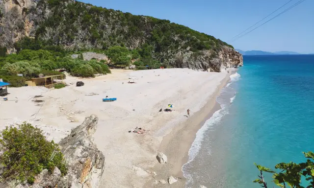 Malownicza plaża Gjipe z turkusową wodą, skalistymi klifami i kilkoma turystami relaksującymi się na piasku.