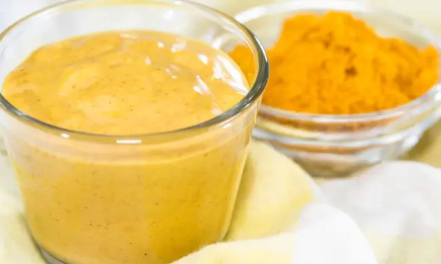 Sauce curry onctueuse dans un verre, avec une coupelle de poudre de curcuma à côté. Parfait pour relever vos plats.