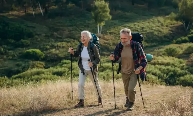 Uśmiechnięta para seniorów z plecakami przemierza leśny szlak, ucząc się, jak chodzić z kijkami.