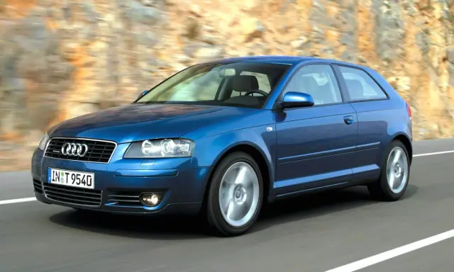 Niebieskie Audi A3 8P w ruchu, z widocznymi przednimi żarówkami, pędzi po drodze wśród skalistych zboczy.