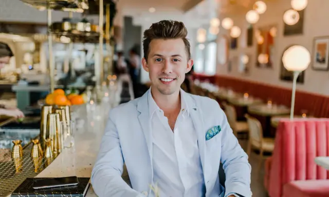 Uśmiechnięty menedżer firmy w jasnoniebieskiej marynarce siedzi przy barze w eleganckiej restauracji.