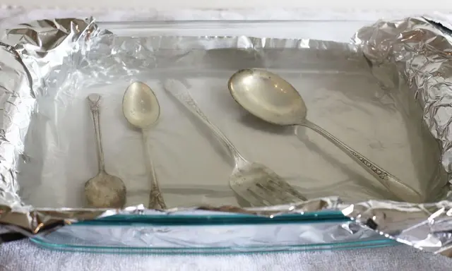 Srebrne sztućce w szklanej misce wyłożonej folią aluminiową.