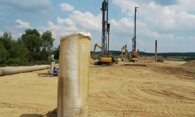 Construcción en terreno arenoso, con maquinaria pesada y tuberías. Se aprecian varios tipos de suelos blandos, listos para la obra.