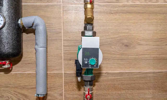 Nowoczesna pompa cyrkulacyjna a obiegowa z cyfrowym wyświetlaczem i pokrętłem regulacji, zamontowana na rurach instalacji grzewczej.