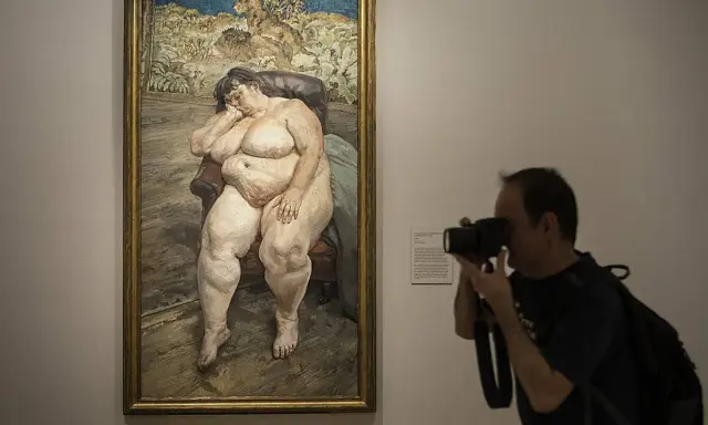 Un hombre fotografía un cuadro de **lucian freud desnudos**, una figura sentada en un sillón, capturando la intimidad de la obra.