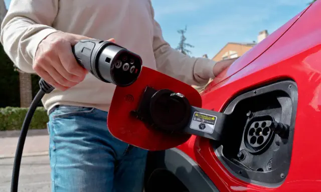 Persona desconectando el cargador de un coche eléctrico rojo.