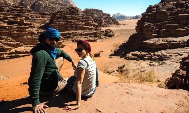 Para w turbanach odpoczywa na piasku, podziwiając skaliste krajobrazy pustyni Wadi Rum.