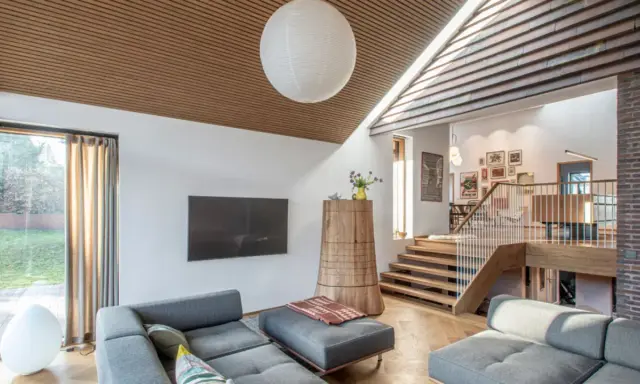 Modernes Wohnzimmer mit grauem Sofa und einem interessanten **split level** Design, das durch eine Holztreppe und einen offenen Wohnbereich gekennzeichnet ist.